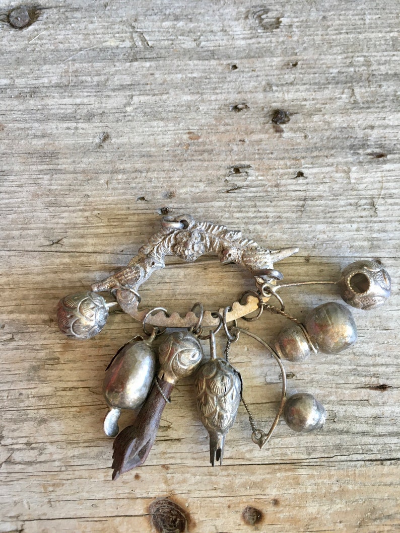 May include: A silver charm bracelet with a variety of charms, including bells, a bird, and a small wooden figure. The bracelet is on a wooden background.