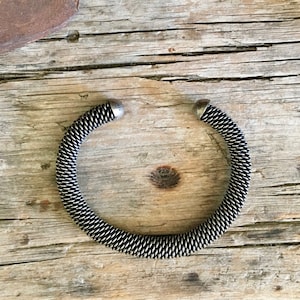 May include: A silver-toned metal bracelet with a coiled design. The bracelet is open and has rounded ends.