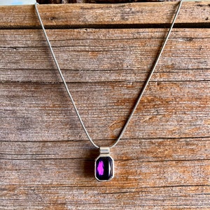 May include: A silver chain necklace with a pendant featuring a dark purple gemstone set in a silver frame.