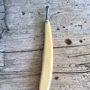 May include: A vintage straight razor with a yellow bone handle. The razor is closed and has a pointed tip.