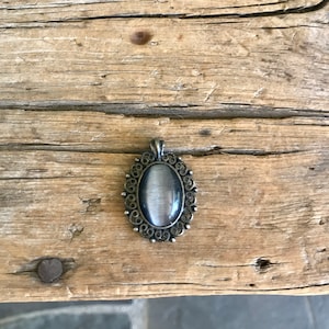 May include: A silver oval pendant with a gray cat's eye stone set in a filigree design.