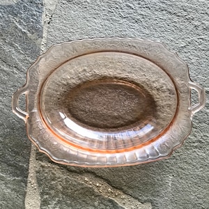 May include: A vintage pink glass serving dish with a scalloped edge and two handles. The dish has a delicate floral pattern.