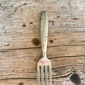 May include: A silver fork with a floral design on the handle. The fork is sitting on a wooden surface.