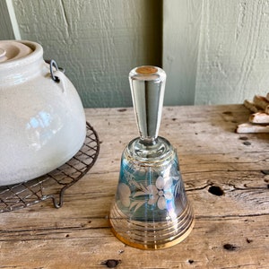 May include: A blue glass bell with a gold rim and etched floral design. The bell has a clear glass handle.