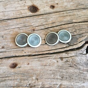 May include: Four silver cufflinks with a white border and a concentric circle design.