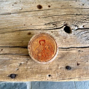 May include: A round, wooden box with a painted image of a couple in traditional clothing. The box has a gold-colored background and the couple is painted in red and orange hues.
