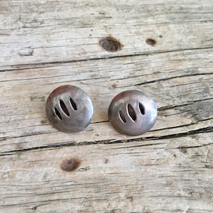 May include: A pair of silver earrings with a cut-out design. The earrings are round and have a slightly textured surface.
