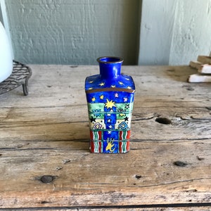 May include: A small, blue, rectangular vase with a star and floral design. The vase is decorated with yellow, green, pink, and red enamel.