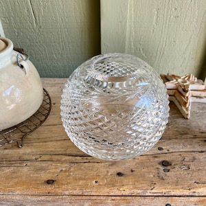 May include: A clear glass vase with a diamond pattern. The vase is round and has a wide opening.