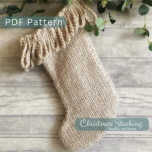 May include: A knitted beige Christmas stocking with a fringed cuff. The stocking has the text "Christmas Stocking" and "Monkey and Minnie" printed on it.