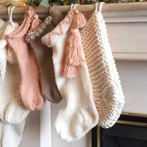 Neutral Boho Christmas stocking hand knitted in soft hues of cream and peach designed to seamlessly harmonise with your home decor. Hand knitted in soft chunky yarn this family stocking has peach detailing and long boho tassels.