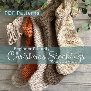 Puede incluir: Tres calcetines de Navidad de punto en beige, marrón y naranja con un detalle de flecos. Los calcetines están colgados en una superficie de madera con vegetación en el fondo. El texto "Beginner Friendly Christmas Stockings Monkey and Minnie" se muestra en una pancarta azul.