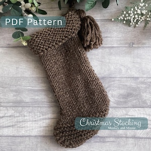 May include: A brown knitted Christmas stocking with a brown tassel. The stocking has a folded cuff and a pointed toe. The text "Christmas Stocking" and "Monkey and Minnie" is printed on the stocking.