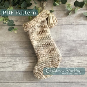 May include: A knitted Christmas stocking in beige and brown tones, with a matching tassel. The text "PDF Pattern" is at the top, and "Christmas Stocking" is at the bottom. The stocking hangs against a wooden background.