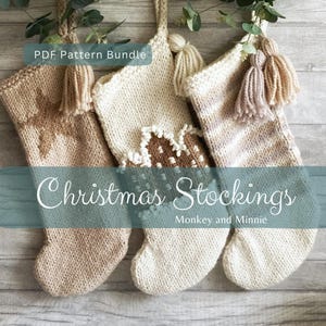 Op de afbeelding: Drie handgebreide kerstsokken met een PDF Pattern Bundle. De linker sok is beige, de middelste is crème met een bruin peperkoekhuisje-ontwerp en de rechter is gemaakt van gemêleerd crème en beige garen. Elke sok heeft een kwastje.