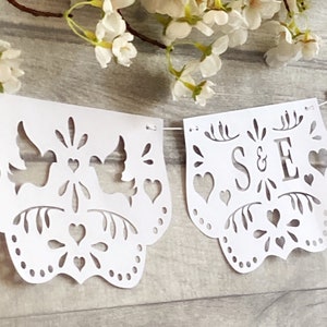 May include: White paper banner with cut-out designs, including doves, hearts, and leaves. The banner reads "S&E" in a decorative font.
