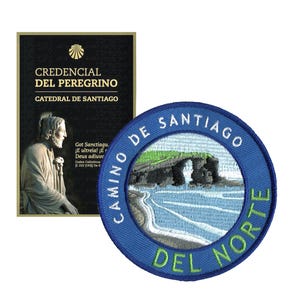 May include: A blue embroidered patch with the text "Camino de Santiago Del Norte" encircling a coastal landscape. Beside it, a black and gold credential with text in Spanish, including "Credencial del Peregrino".