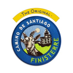 May include: Embroidered patch with a blue circular design featuring a goat, a building, and the words "CAMINO DE SANTIAGO FINISTERRE." A yellow banner above reads ".THE ORIGINAL."
