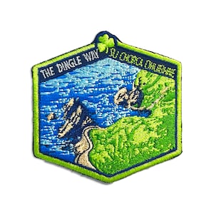 May include: An embroidered patch in green, blue and white with a shamrock in the top left corner. The patch features a stylised image of a coastline with the text "The Dingle Way" and "I ♥ Dingle Peninsula" in white.