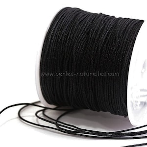 Puede incluir: Una bobina de cordón encerado negro, un tipo de cuerda utilizada para la elaboración de joyas y manualidades. El cordón está enrollado alrededor de una bobina de plástico blanco con el sitio web "www.perles-naturelles.com" impreso en el lateral.