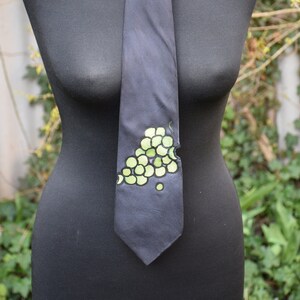 May include: A dark blue tie with a green grape design. The tie is tied around a black mannequin.
