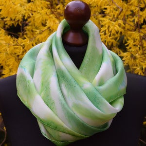 May include: A green and white silk scarf with a hand-painted abstract design. The scarf is draped over a wooden mannequin head.