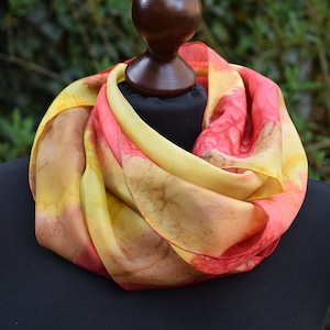 May include: A yellow and red silk scarf with a marbled pattern. The scarf is draped around a wooden mannequin head.