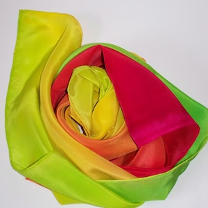 May include: A vibrant, multi-colored silk scarf. The scarf is arranged in a spiral, showcasing a gradient of colors from lime green to hot pink. The fabric appears smooth and lustrous, suggesting a high-quality material.