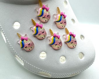 May include: Six pink, blue, and yellow glitter unicorn charms with pink bows. The charms are on a white surface.