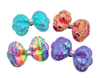 May include: Four iridescent sequin hair bows in blue, pink, rainbow, and purple. Each bow has a pearl in the center.