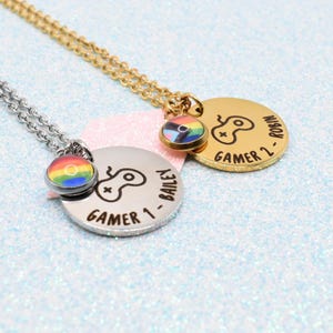 May include: Two gamer necklaces with round pendants and rainbow-colored charms. One pendant is silver with "Gamer 1 - Bailey" and a game controller icon. The other is gold with "Gamer 2 - Robin" and a controller icon.