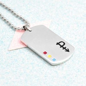 Peut inclure: Pendentif en forme de plaque d'identité argenté, avec une chaîne à billes. La plaque comporte un symbole noir et trois petits carrés colorés : rouge, jaune et bleu. Un accessoire élégant.