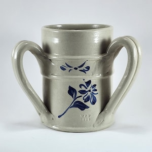 May include: A stoneware pitcher with two large handles. The light gray pitcher features blue floral designs and the text "WPV 1993". The pitcher has a cylindrical shape with a wide opening.