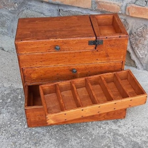 May include: A wooden box with multiple drawers and compartments. The box is open, revealing the compartments inside. The box is made of a light brown wood and has a natural finish.