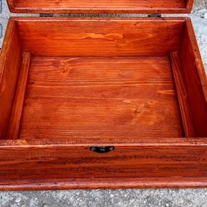 May include: A wooden box with a hinged lid and a metal latch. The box is open and the inside is empty. The box is made of dark wood and has a natural finish.