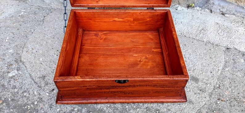 May include: A wooden box with a hinged lid and a metal latch. The box is open and the inside is empty. The box is made of dark wood and has a natural finish.