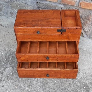 May include: A wooden box with three drawers and a hinged top. The box is made of dark wood and has a natural finish. The drawers are all open and show the interior of the box.