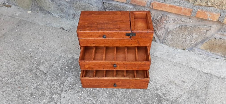 May include: A wooden box with three drawers and a hinged top. The box is made of dark wood and has a natural finish. The drawers are all open and show the interior of the box.