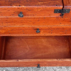 May include: A wooden chest with three drawers, each with a black metal knob. The top drawer is closed, the middle drawer is open, and the bottom drawer is closed.