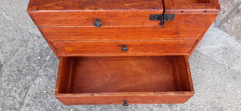 May include: A wooden chest with three drawers, each with a black metal knob. The top drawer is closed, the middle drawer is open, and the bottom drawer is closed.