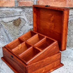May include: A wooden box with a hinged lid and multiple compartments. The box is stained a rich reddish-brown colour.