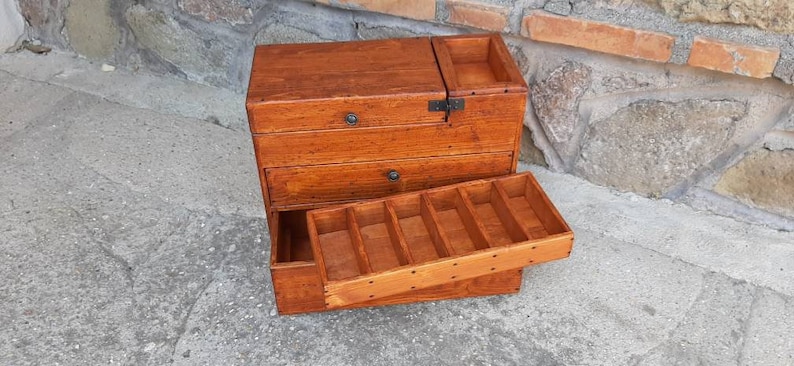 May include: A wooden box with multiple drawers and compartments. The box is open, revealing the compartments inside. The box is made of a light brown wood and has a natural finish.