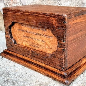 May include: A wooden box with a hinged lid and a decorative inscription on the front. The inscription reads "YOUR INSCRIPTION HERE" and includes the alphabet in a decorative font. The box is stained a dark brown color and has a base.