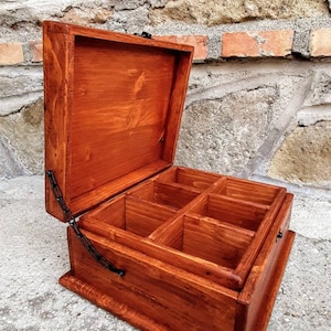 May include: A wooden box with a hinged lid and a metal chain closure. The box has six compartments inside and is stained a rich brown colour.