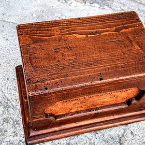 May include: A wooden box with a hinged lid and a small opening on the front. The box is made of dark brown wood and has a natural finish. The box is about 10 inches long, 6 inches wide, and 4 inches tall.