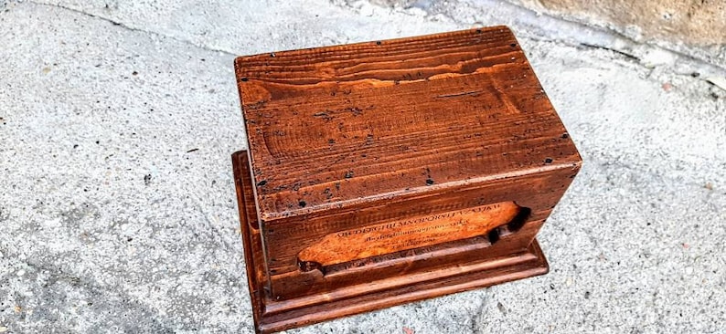 May include: A wooden box with a hinged lid and a small opening on the front. The box is made of dark brown wood and has a natural finish. The box is about 10 inches long, 6 inches wide, and 4 inches tall.