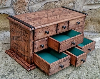 May include: A wooden box with multiple drawers, each lined with green felt. The box has a distressed finish and black metal accents.