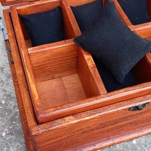May include: A wooden box with a hinged lid and a metal clasp. The box is divided into compartments lined with black fabric. The box is made of light brown wood and has a natural finish.