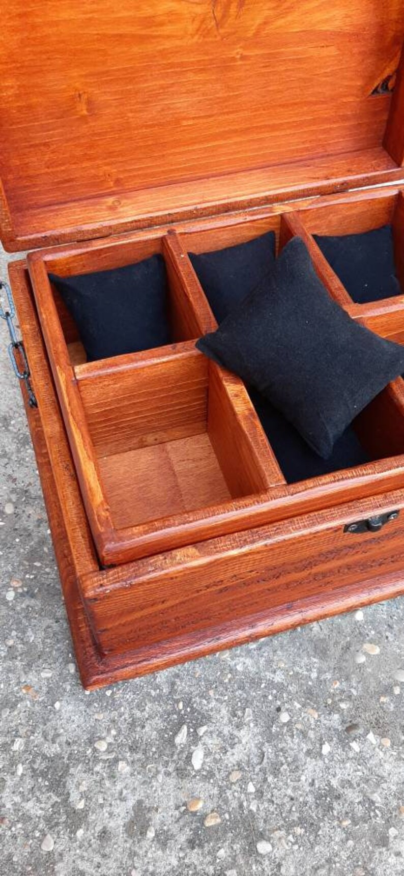 May include: A wooden box with a hinged lid and a metal clasp. The box is divided into compartments lined with black fabric. The box is made of light brown wood and has a natural finish.