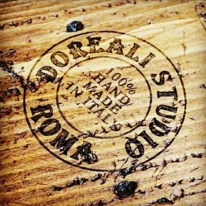 May include: A close-up of a wooden surface with a circular stamp that reads "D'OREALI STUDIOS ROMA 100% HAND MADE IN ITAL".